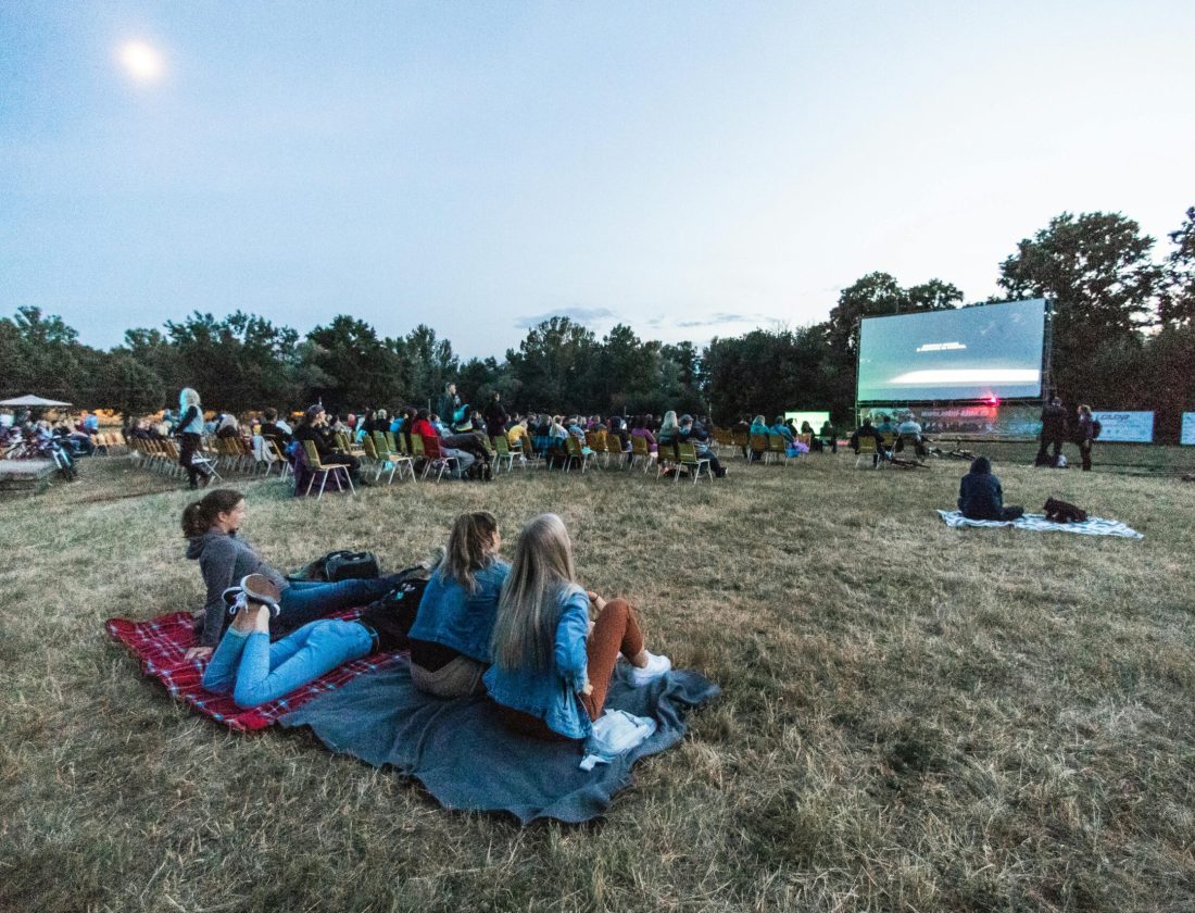 People enjoying an outdoor movie night under the sky in a scenic setting surrounded by trees.